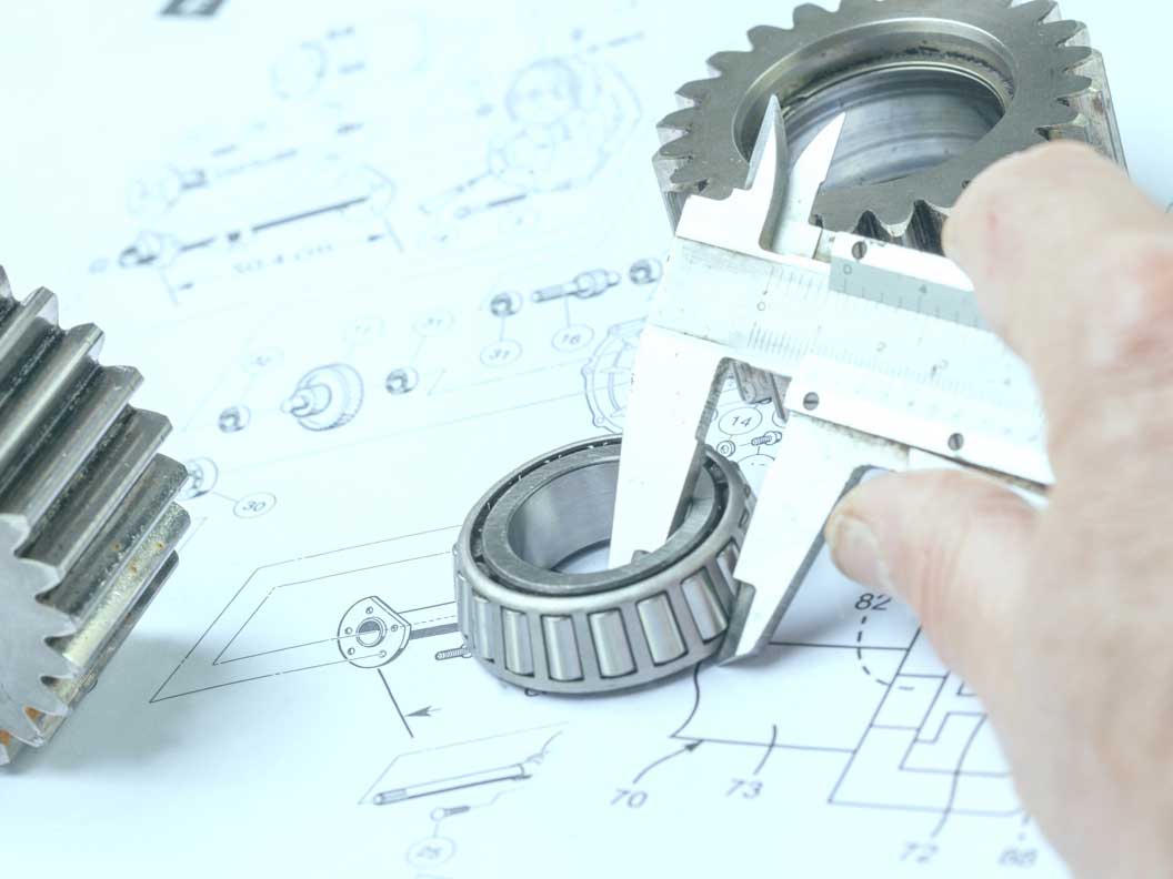 Close-up of a mechanical engineering technician using calipers to measure gear dimensions.