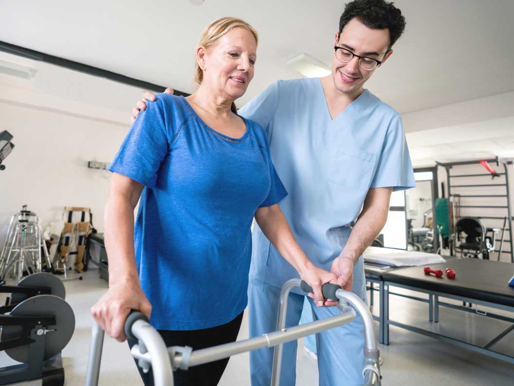 Male physical therapy assisstant helps a female patient with her walker. 