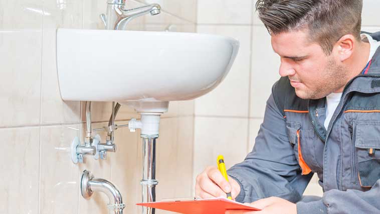Male plumber inspects a bathroom faucet to prepare a cost estimate. 