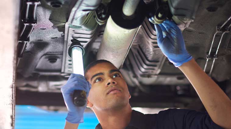 Automotive body repairman inspects a car undercarriage for structural damage. 