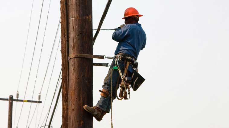 Male power-line repairer works on repairing electrical power-line pole. 