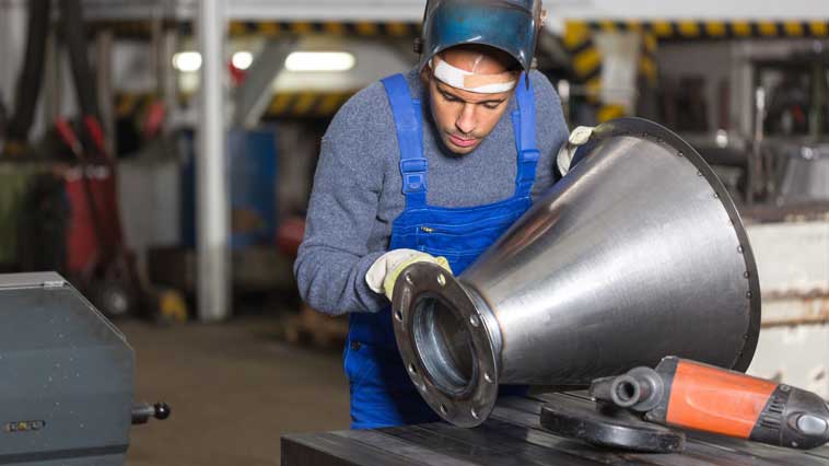 Male welder inspects metal cone to be welded. 